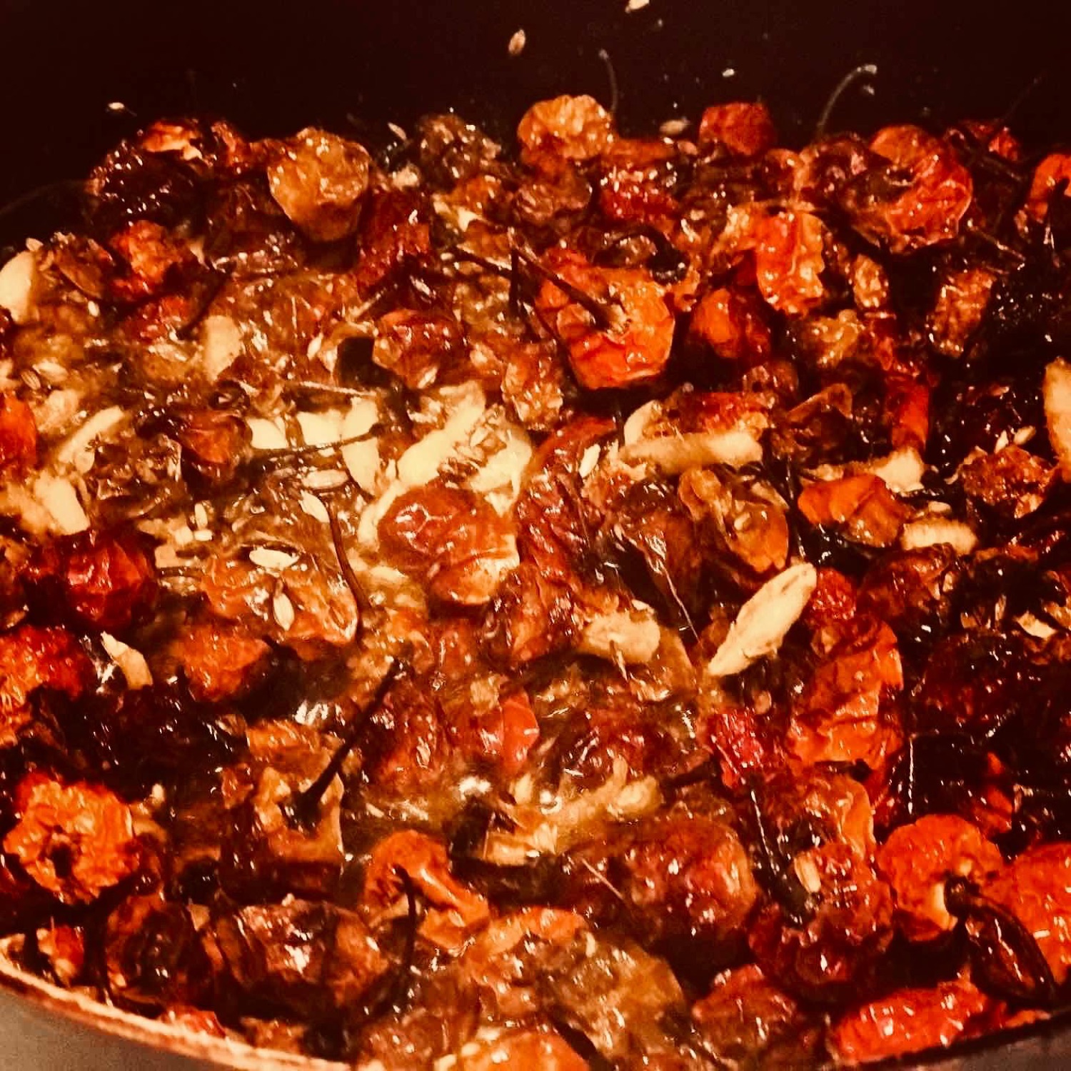 Dried tomatoes and chilies cooking down with spices in a dark pan