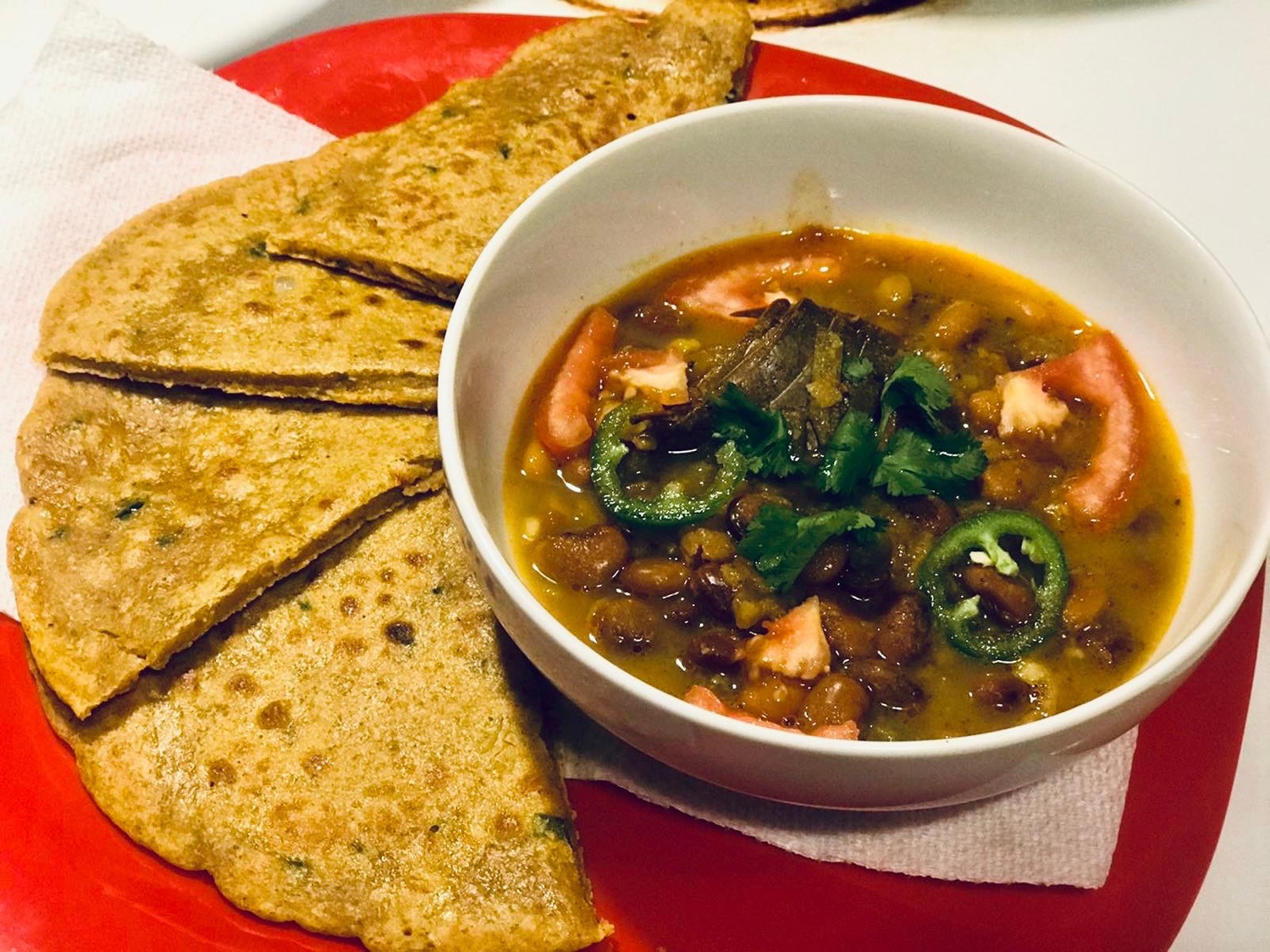Quartered paratha beside a bowl of bean curry with tomato and jalapeño