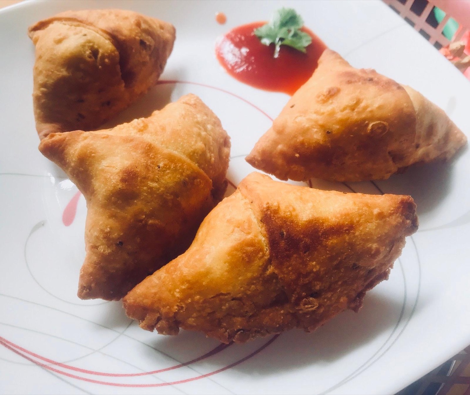 Four golden samosas on a plate with ketchup