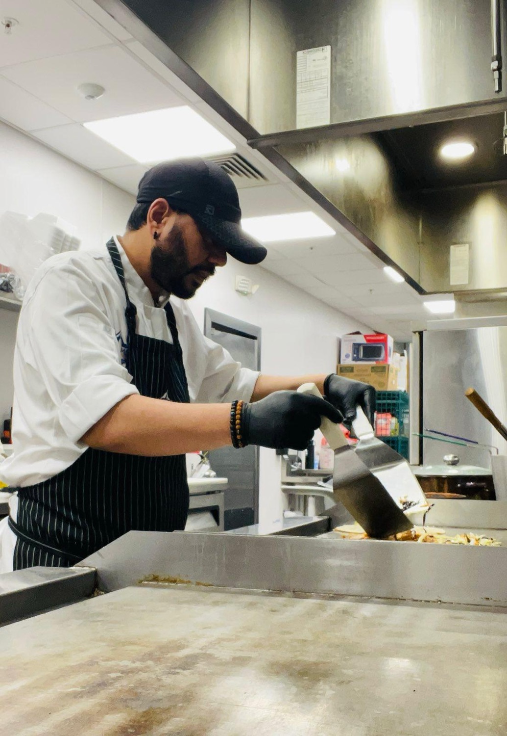 Udeep in chef whites and a pinstripe apron working at a flat-top griddle