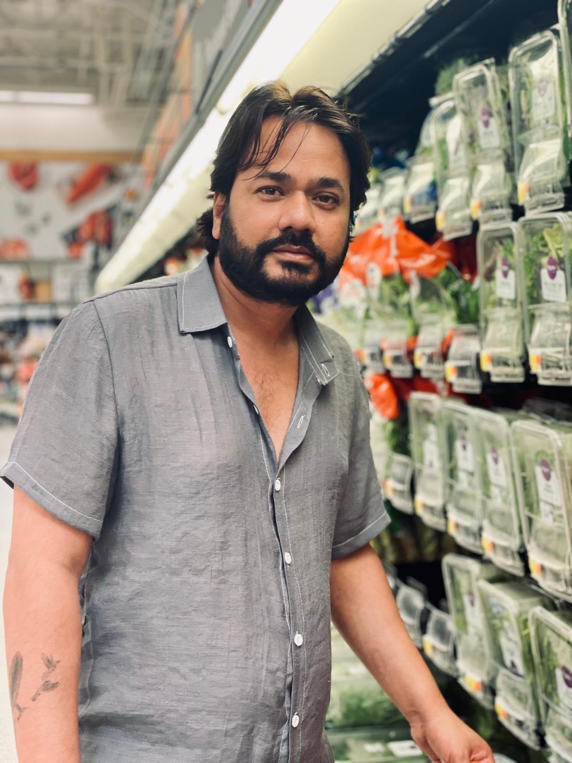 Udeep in a grey linen shirt standing by the fresh herbs aisle