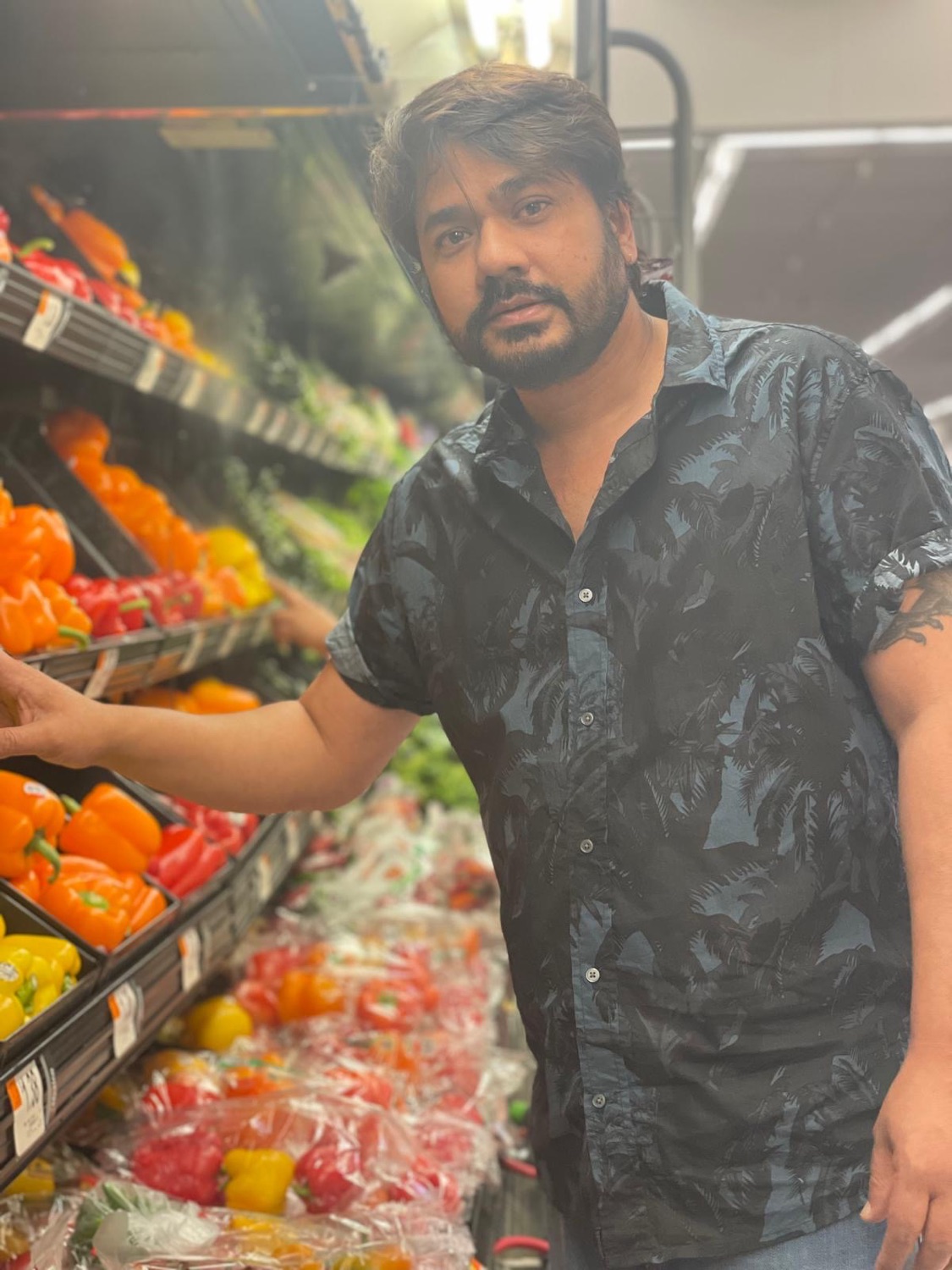 Udeep in a supermarket produce aisle with a hand on the bell pepper shelf