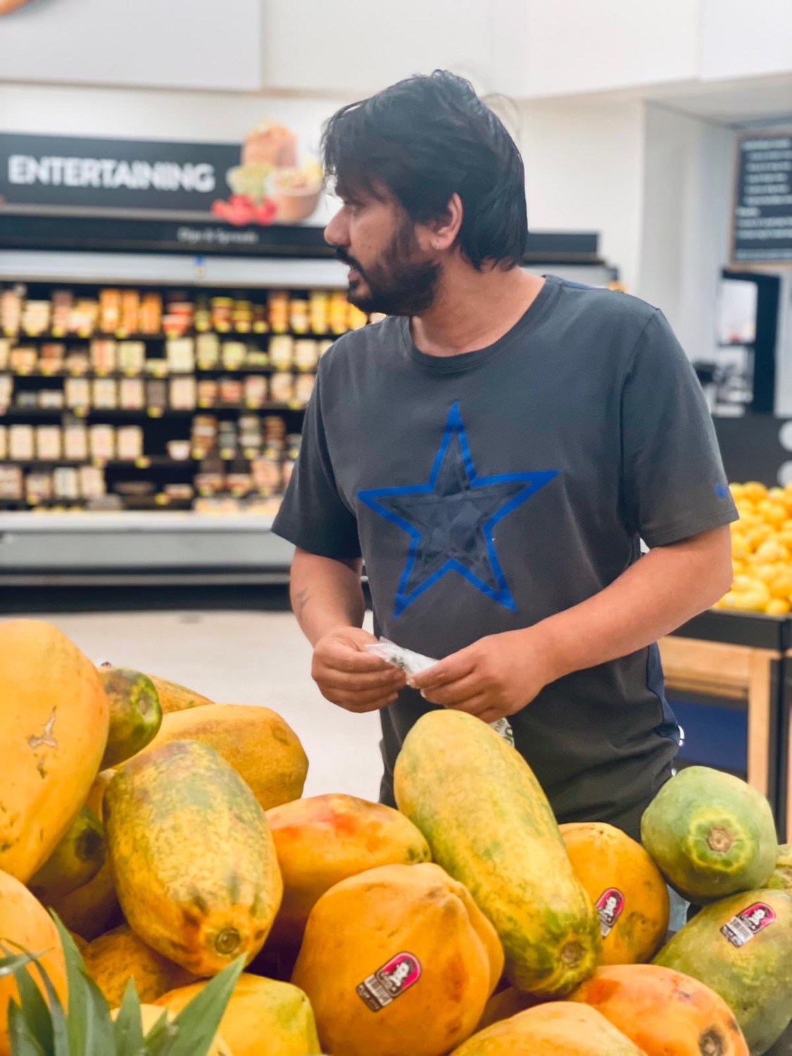 Udeep beside a large pile of papayas in a grocery store